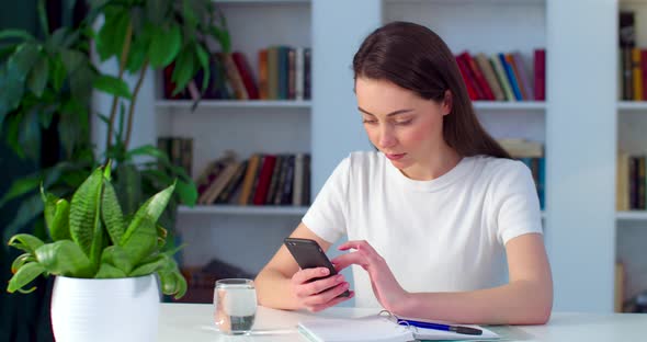 Concentrated Woman Surfing Internet on Smartphone Sitting at Table Indoors
