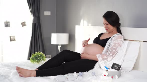 pregnant woman looking and pats her belly on the bed