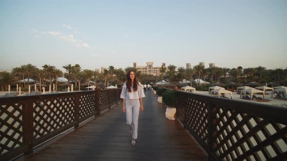 Front View of Woman Walking on Wooden Pier in Luxury Tourist Resort in Dubai alt