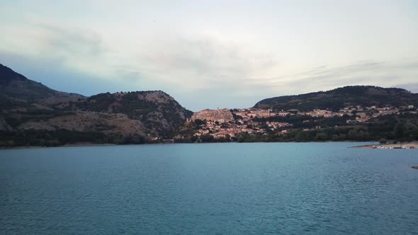 Aerial Panning Shot of Trees at Lakeshore Near Mountain Range Drone Flying Forward Over Lake Against alt