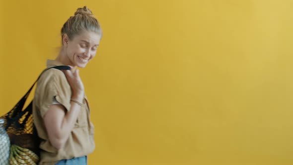 Slow Motion of Happy Girl Carrying Reusable Bag with Food on Yellow Background alt