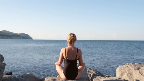 Girl Sits in a Lotus Position in Black Swimsuit on the Seashore Looks at the Sea Dawn of the Sun alt
