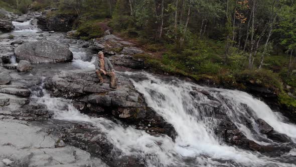 Tourist Sitting on a Giant Boulder in the Middle of a Turbulent Mountain Stream