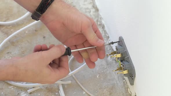 A Male Electrician Makes Electrical Wiring in the Wall Screwing the Wires and the Socket to the Wall