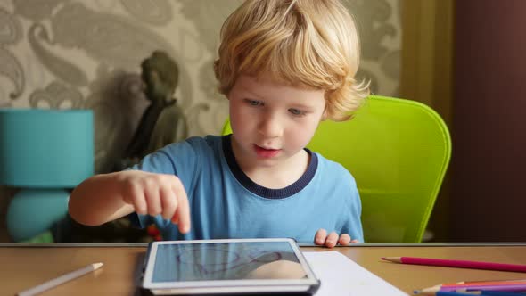 Young Blonde Boy Using His Computer Tablet For Creative Drawings By Hand. alt