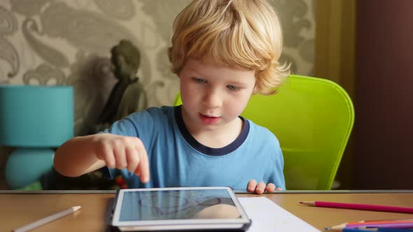 Young Blonde Boy Using His Computer Tablet For Creative Drawings By Hand.
