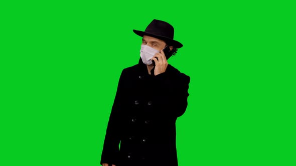 Stylish Man In Black Hat And Protective Mask Talking On Phone against Green Screen