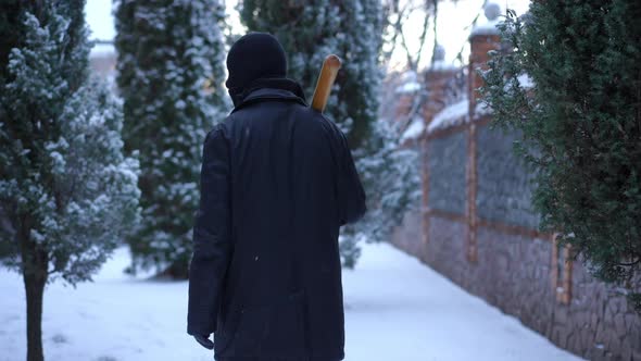 Back View Burglar with Baseball Bat Walking on Snowy Backyard Outdoors alt