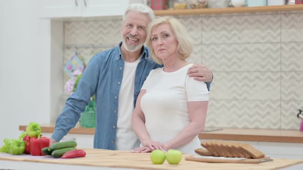 Loving Old Couple Looking at Camera in Kitchen alt