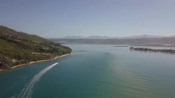High aerial in Knysna Lagoon as speed boat cuts white wake in water alt