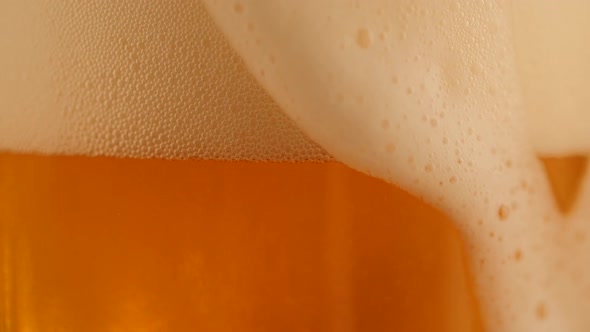 Detail of Pouring Fresh Beer with Foam Running Down Golden Background alt