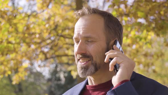 A Middleaged Handsome Caucasian Man Talks on a Smartphone in a Park in Fall  Closeup