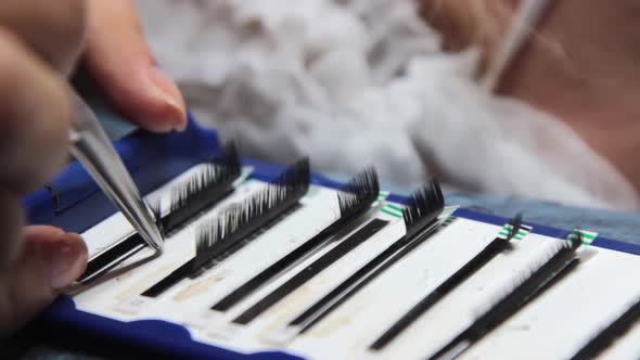 the Master Takes the Eyelashes From the Package for Gluing to the Patient with Tweezers alt