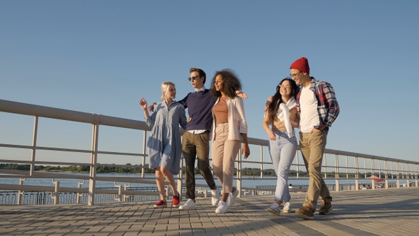 Diverse young smiling friends walking on warm day having alt