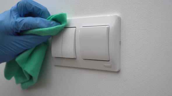 A Cleaner Man Wearing Gloves and a Mask Disinfects Electrical Light Switches  to Prevent COVID 19 alt