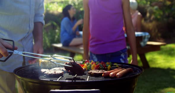 Grandfather and granddaughter preparing barbecue while family having meal 4k alt