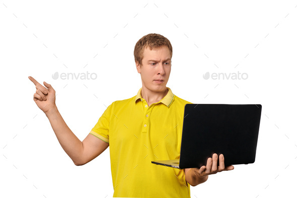 Puzzled young man with laptop pointing with finger isolated on white background, male confused face - Stock Photo - Images