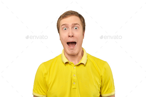 Surprised young man with funny facial expression in yellow T-shirt, white isolated background - Stock Photo - Images