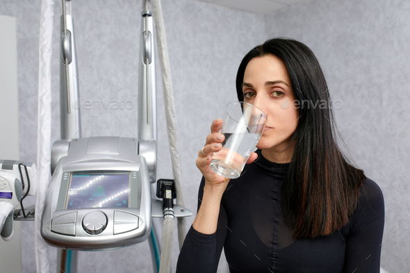 woman in a black suit for LPG massage drinking water before LPG massage. Anti-cellulite body care