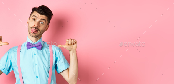 Funny guy in suspenders and bow-tie showing tongue, pointing at himself as if self-promoting