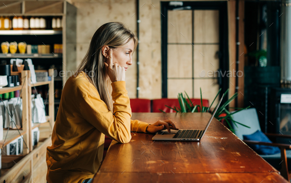 Business woman working on a laptop while sitting at a table in a coffee house. - Stock Photo - Images