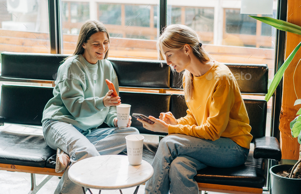 Two cheerful laughing women friends in a coffee shop communicate and chat on the phone. - Stock Photo - Images