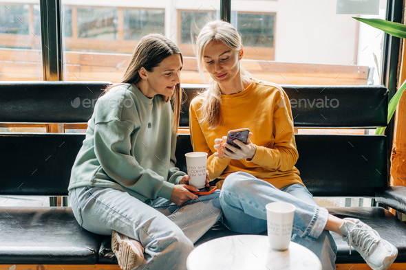 Two modern confident women friends in a coffee shop communicate and chat on the phone. - Stock Photo - Images
