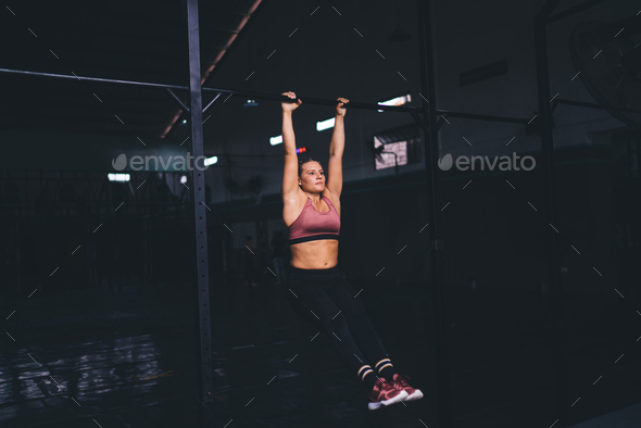 Muscular female athlete training body muscles while doing pull ups in ...