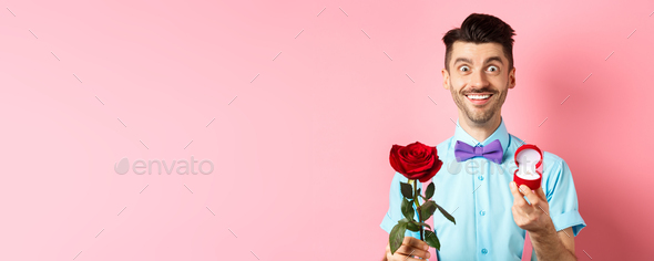 Valentines day. Smiling handsome man asking to marry him, showing engagement ring and red rose