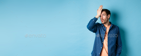 Annoyed man making facepalm and roll eyes from something stupid, standing over blue background with