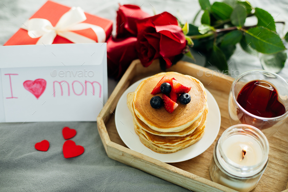 Wooden tray with delicious breakfast - syack of pancakes, tea, present, roses and burning candle - Stock Photo - Images