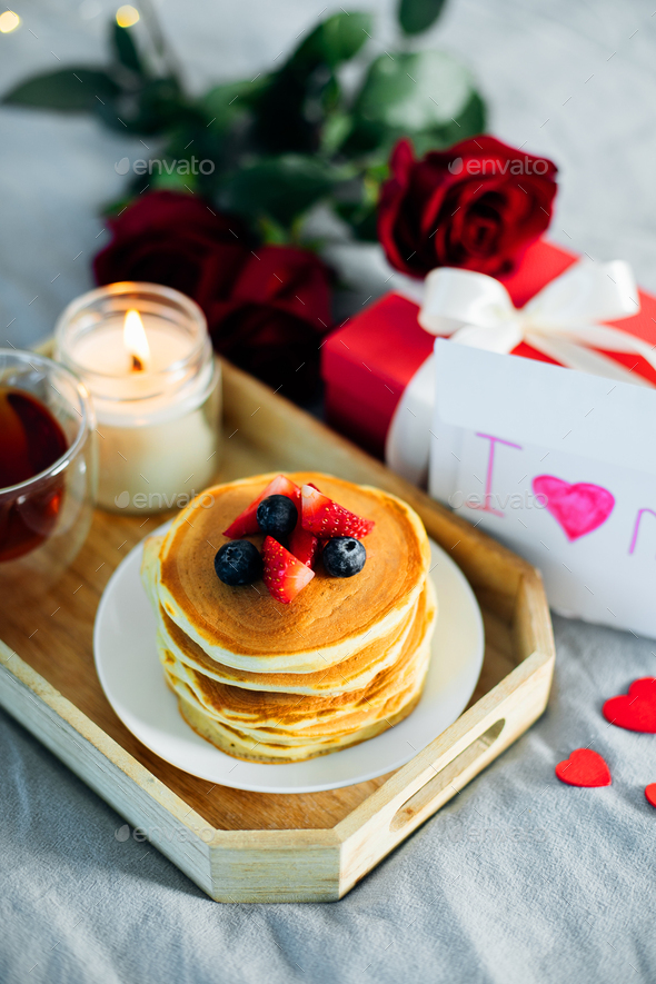 Mother's Day concept. Pancakes with berry, tea cup, burning candle, flowers and gift box. - Stock Photo - Images