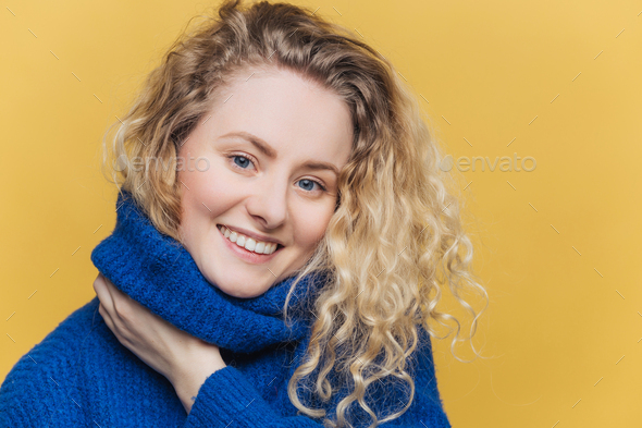 Close up shot of delighted satisfied female model has curly blonde hair, broad smile - Stock Photo - Images