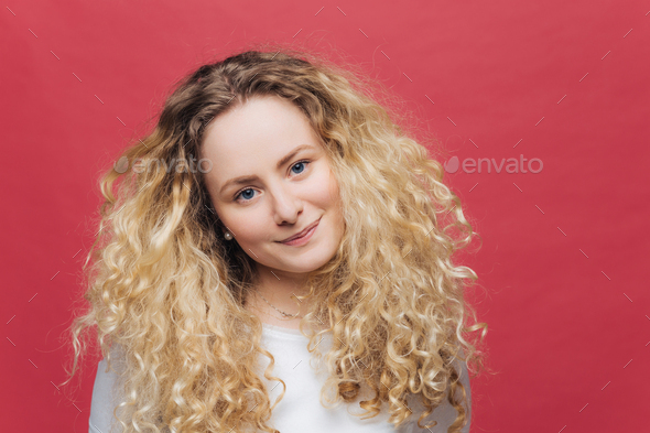 female with curly bushy hair and blue eyes, looks positively at camera, feels satisfied as meets wit - Stock Photo - Images