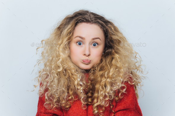 blonde female with curly hair, blows cheeks and stares at camera, reacts actively on unexpected news - Stock Photo - Images