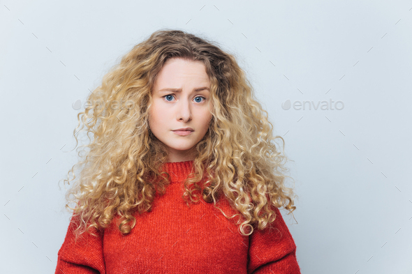 displeased unhappy young woman with curly bushy blonde hair, frowns face in bewilderment - Stock Photo - Images