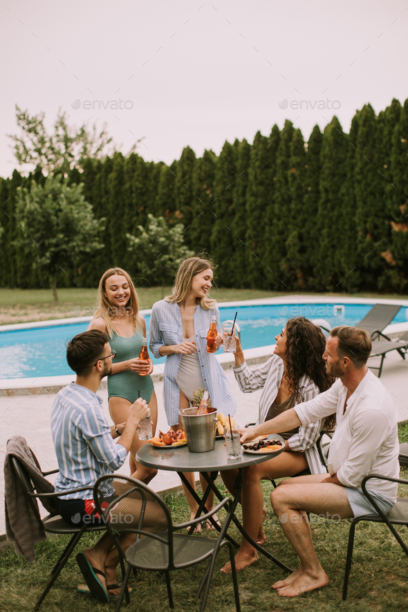 Group of young people cheering with cider by the pool in the garden - Stock Photo - Images