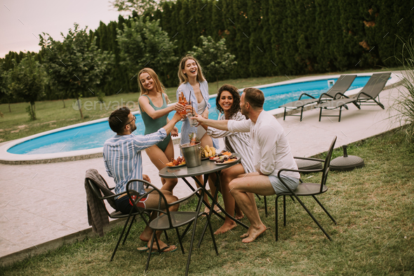 Group of young people cheering with cider by the pool in the garden - Stock Photo - Images