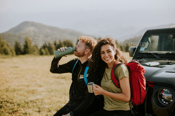 Smiling couple preparing hiking adventure with backpacks by terrain vehicle - Stock Photo - Images