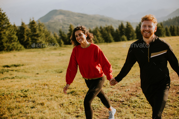 Smiling couple walking over green hills - Stock Photo - Images