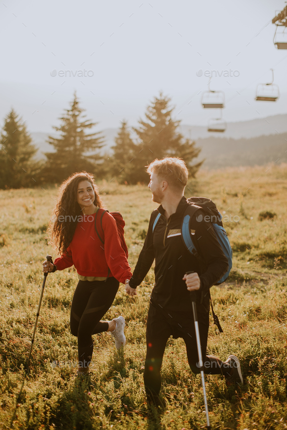 Smiling couple walking with backpacks over green hills - Stock Photo - Images