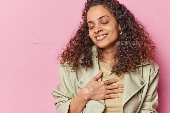 Pleased young woman with Afro hair presses hand to chest feels gratitude being thankful for - Stock Photo - Images