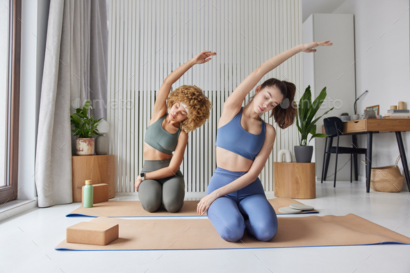 Sporty women practice yoga pose on fitness mat dressed in sportswear leans aside have pilates - Stock Photo - Images
