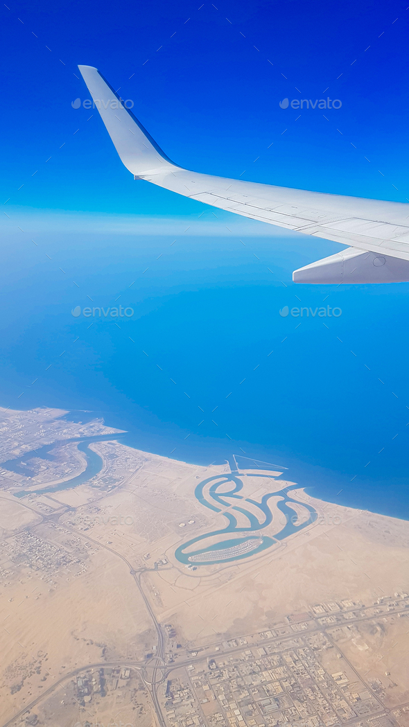 View from the window of plane on blue sky and earth with landscape of desert, sea and canals in