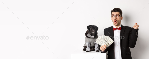 Happy young man in suit earn money with his dog. Guy rejoicing, holding dollars and staring left