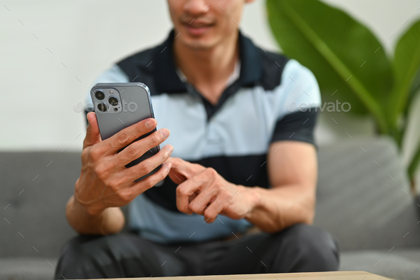 Cropped shot of pleasant man communicating in social network on smart phone and relaxing on sofa. - Stock Photo - Images