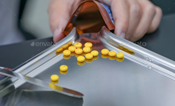 Selective focus on yellow tablets pills on stainless tray with blur hand of pharmacist or pharmacy - Stock Photo - Images