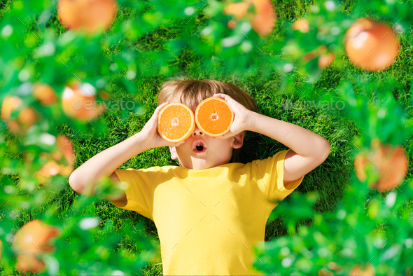 Surprized child holding slices of orange fruit like sunglasses - Stock Photo - Images
