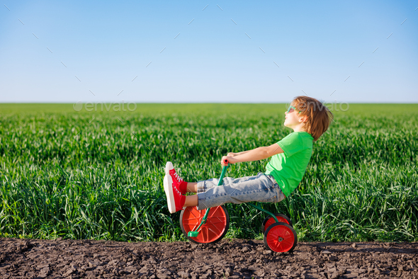Happy child riding bike outdoor in spring green field - Stock Photo - Images