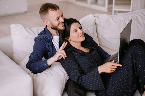 bearded Italian guy in casual sits on couch with wife makes video call by laptop gestures hello